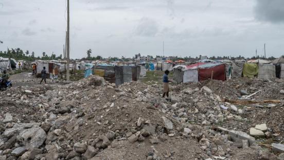 Aftermath of a disaster, with rubble and tents acting as temporary housing