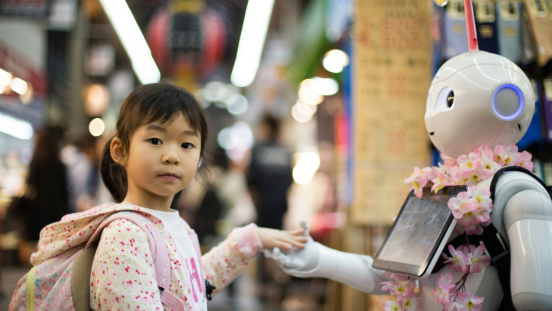 A little girl lays her left hand in the hand of a white robot
